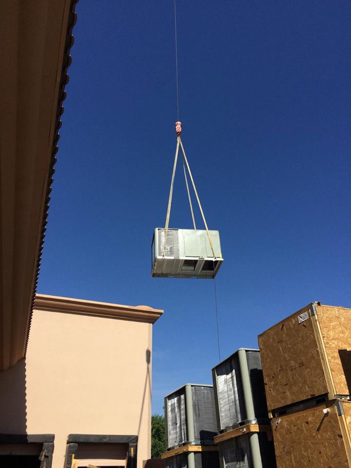 A large HVAC unit being lifted by a crane for installation by Hughes Air Heating & Cooling in Mesa, AZ.