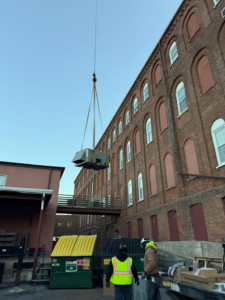 Workers observe an HVAC unit being carefully lifted by a crane during an installation project by JK Mechanical in Willow Street, PA.