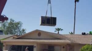 An HVAC unit being lifted by a crane over a residential house for installation by Ash Cooling & Heating in Mesa, AZ.