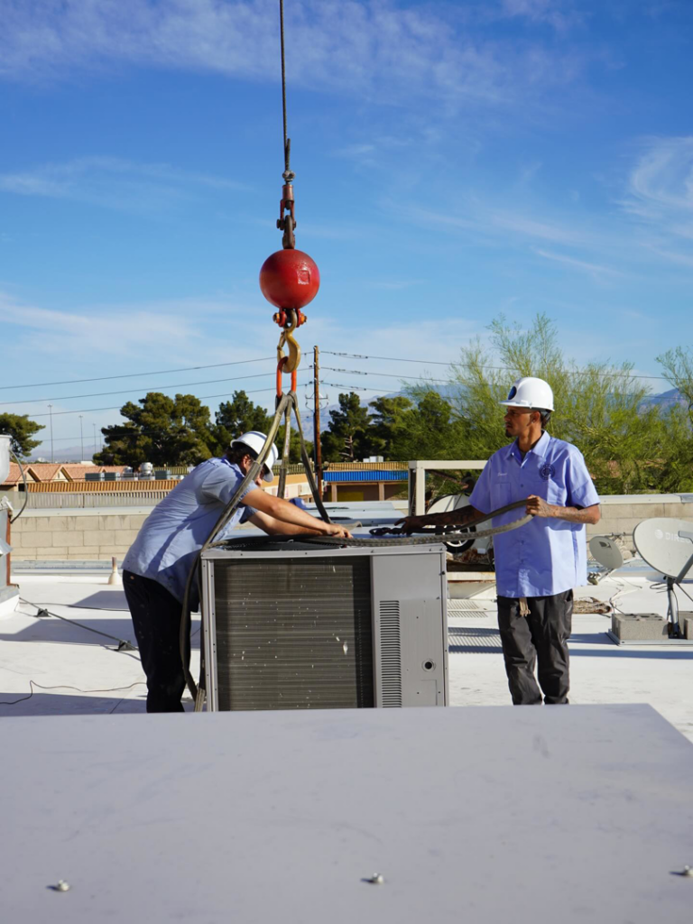 Two HVAC technicians guiding a new unit being installed by crane on a rooftop by Blue Collar HVAC in Henderson, NV.