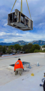A large HVAC unit being installed by crane on a rooftop by Husky Heating and Cooling in Westminster, CO.
