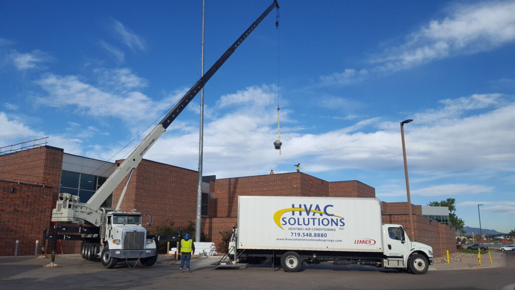 A crane lifting a new HVAC unit onto a commercial rooftop during an installation by HVAC Solutions in Colorado Springs, CO