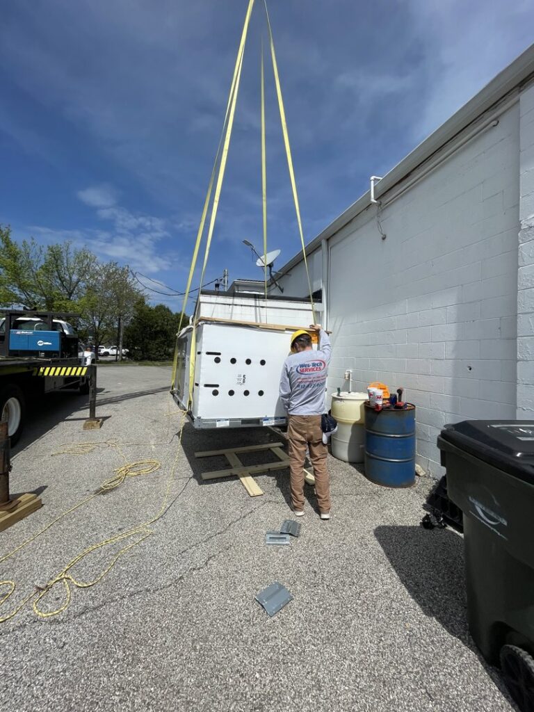 A large HVAC unit being lifted by a crane for installation by Wes-Tech Services in Bloomington, IN.