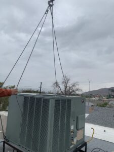 An HVAC unit being lifted by a crane onto a rooftop for installation by EA Heating & Cooling in El Paso, TX.