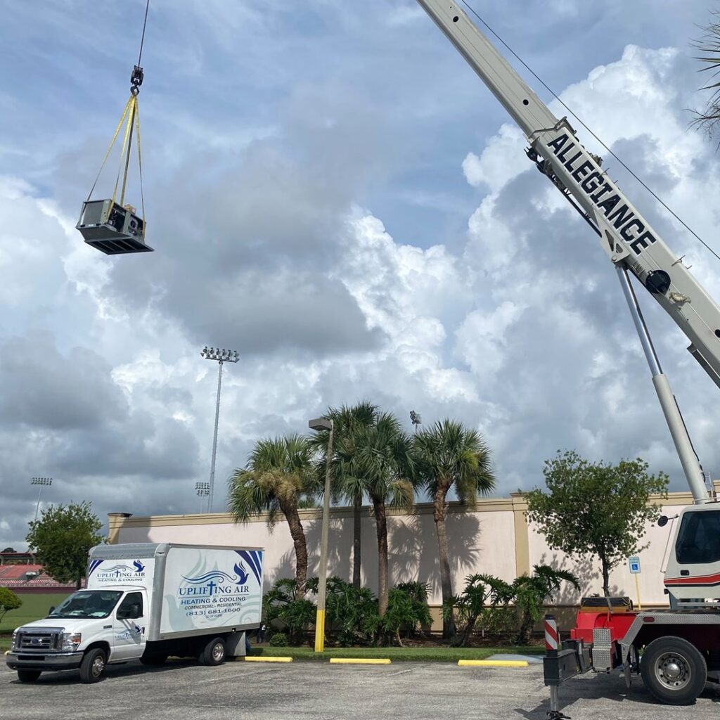 A smaller HVAC unit being lifted by a crane with an Uplifting Air, LLC service truck nearby in San Antonio, FL.