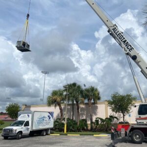 A smaller HVAC unit being lifted by a crane with an Uplifting Air, LLC service truck nearby in San Antonio, FL.