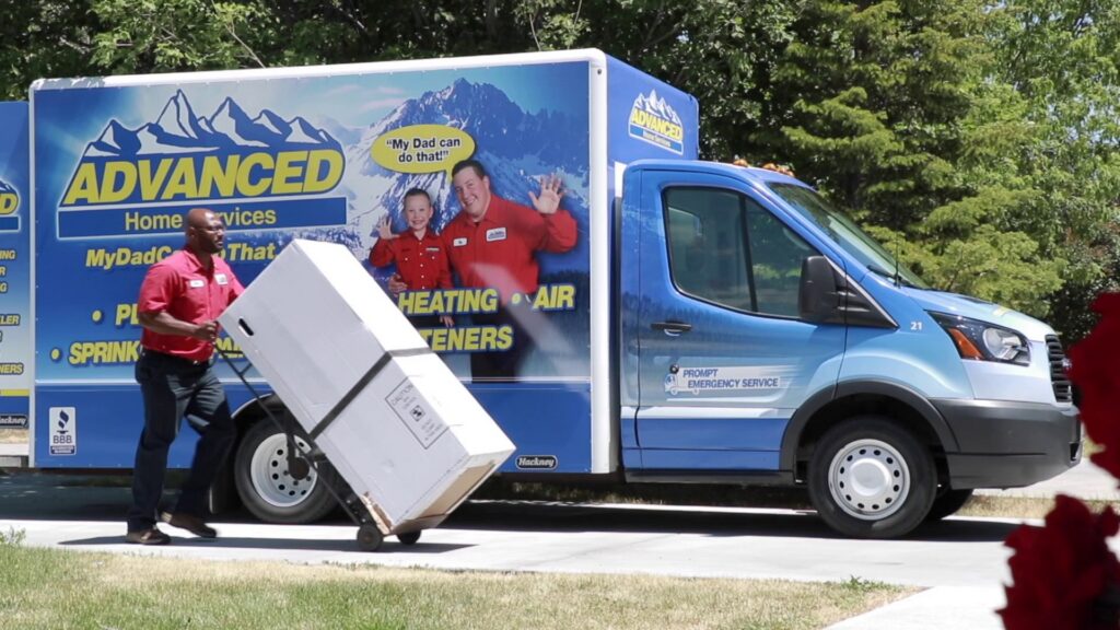 An Advanced Home Services technician delivering a new HVAC unit from a company truck in Rigby, ID.