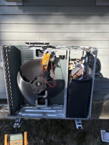 An HVAC technician performing diagnostic and repair service on an outdoor unit with a multimeter by Laird's HVAC in Auburn, ME.