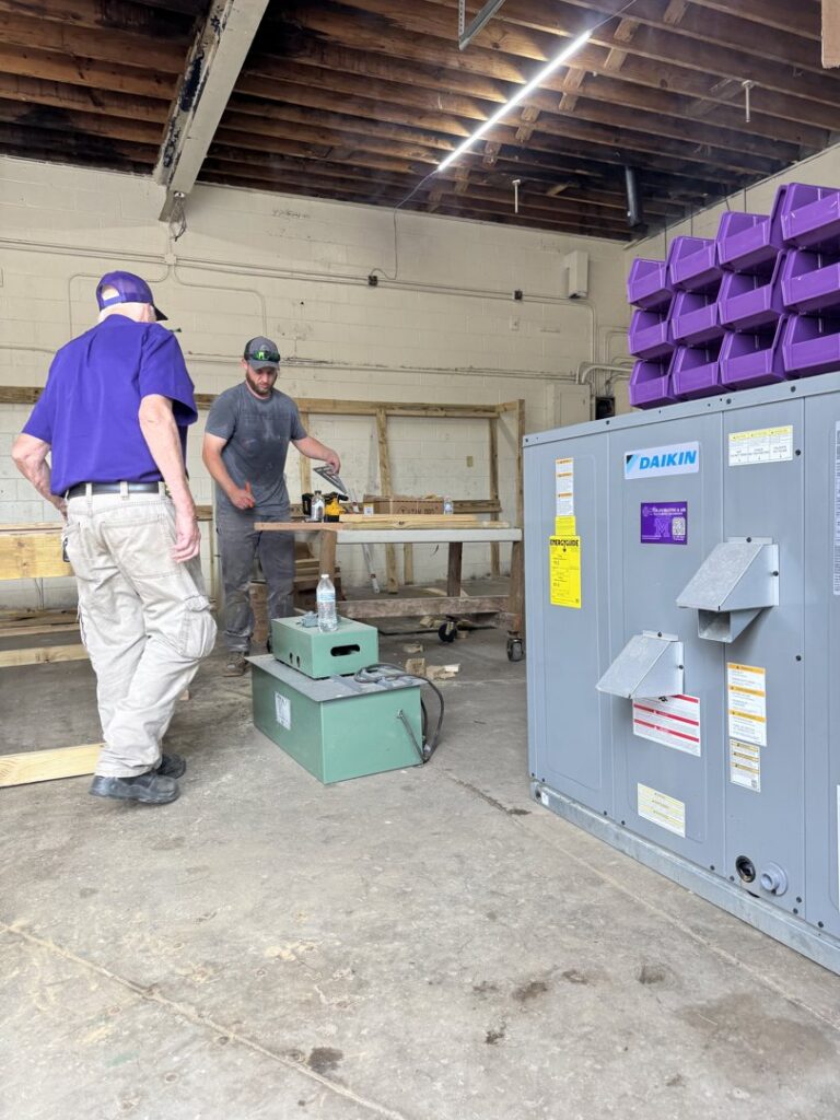 Technicians working in a workshop with a Daikin HVAC unit and fabrication equipment at Milan Heating & Air in Milan, TN.