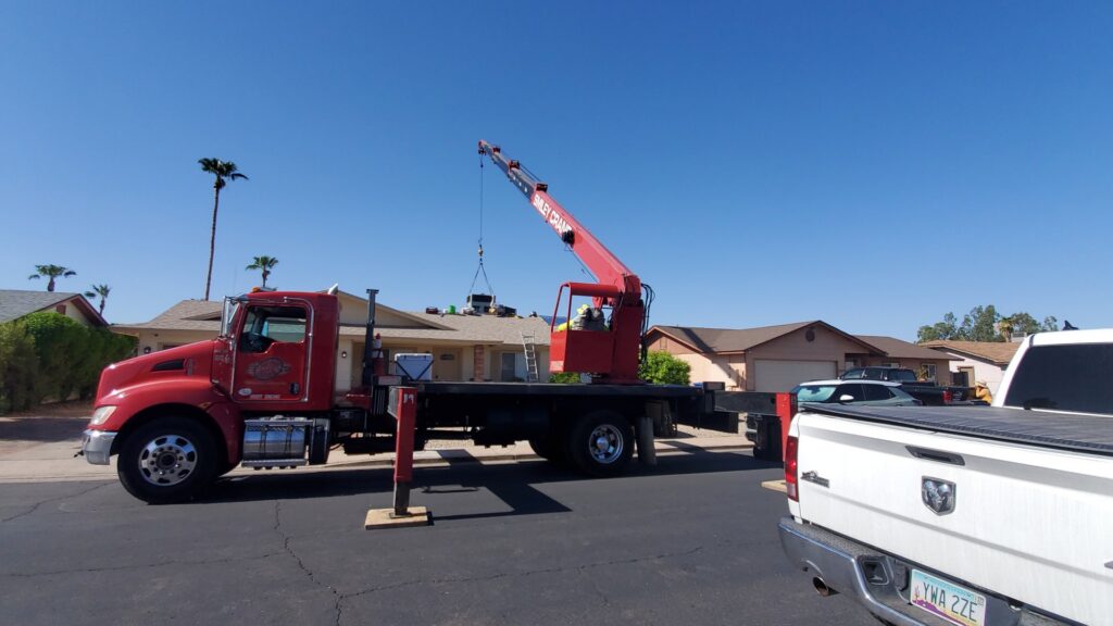 An HVAC unit being hoisted by a crane onto a residential roof for installation by Ash Cooling & Heating in Mesa, AZ.