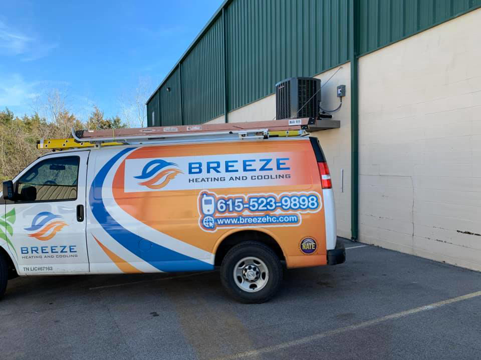 An outdoor HVAC unit installed on a building wall with a Breeze Heating & Cooling Nashville service van nearby in Nolensville, TN.