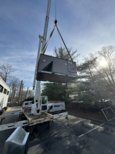 A large HVAC unit being lifted by a crane for installation by Prism Heating & Air Conditioning in Toms River, NJ.
