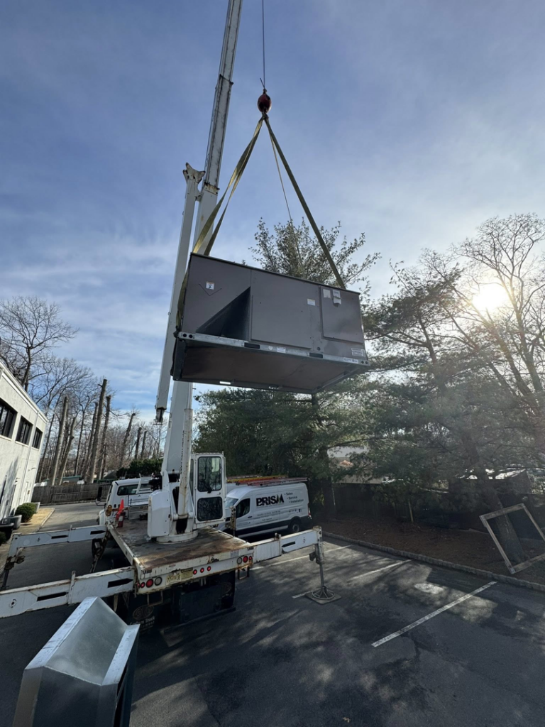 A large HVAC unit being lifted by a crane for installation by Prism Heating & Air Conditioning in Toms River, NJ.