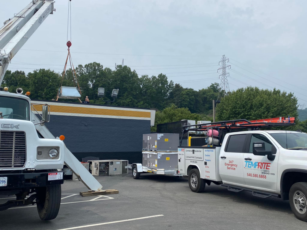A crane lifting a new HVAC unit onto a commercial rooftop, with a Temprite service truck and trailer nearby in Laredo, TX.