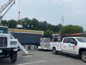 A crane lifting a new HVAC unit onto a commercial rooftop, with a Temprite service truck and trailer nearby in Laredo, TX.
