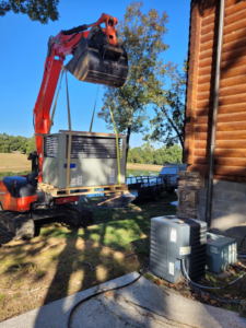 An excavator lifting a large HVAC unit for installation at a property by SleepRite Heating & Cooling in Conway, AR.