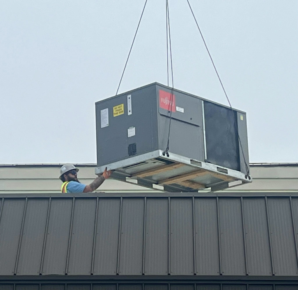 A worker guiding a Fujitsu HVAC unit being installed on a rooftop by Pacifico Heating and Cooling in Shadyside, OH.