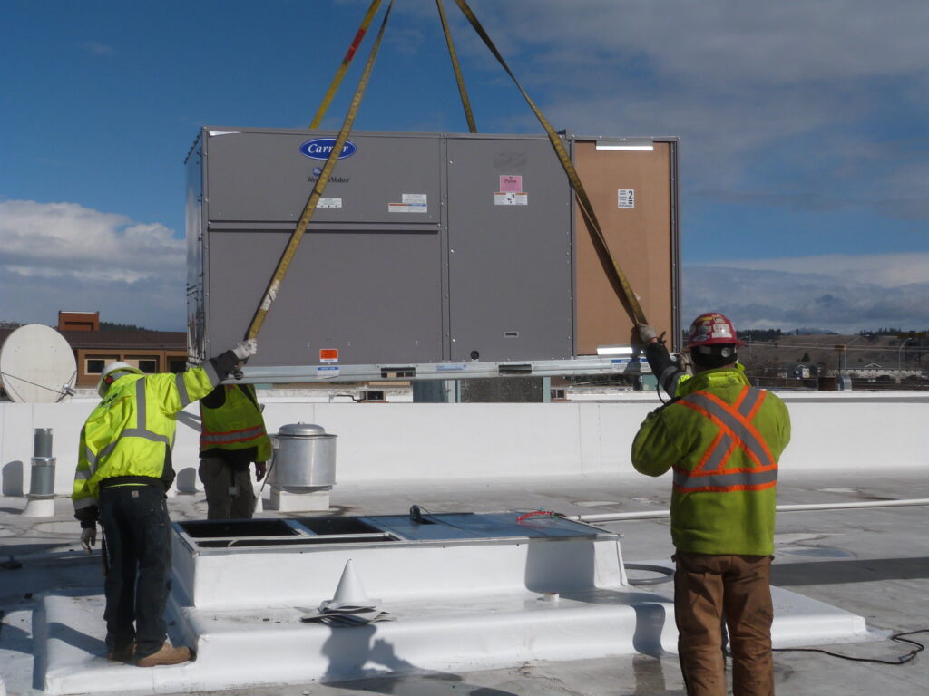 HVAC technicians installing a large Carrier WeatherMaker unit on a commercial rooftop for R&R Heating & Air Conditioning in Spokane, WA.