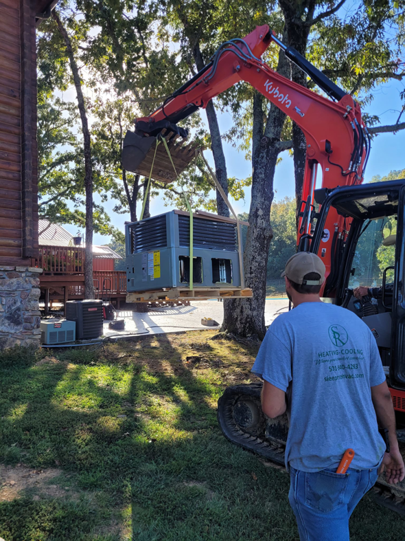 A SleepRite Heating & Cooling technician overseeing the lift of a new HVAC unit by an excavator in Conway, AR.
