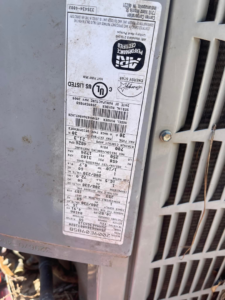 A close-up view of an HVAC unit's technical label, indicating service by Reeds heating and air LLC in Mobile, AL.