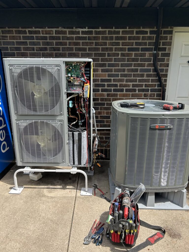 Two outdoor HVAC units, one open for service, with tools nearby from Omega Air Solutions in West Des Moines, IA.