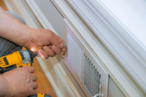 A technician installing an HVAC vent with a power drill, demonstrating service by Basic HVAC in Indianapolis, IN.