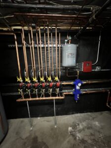 A detailed view of a hydronic heating manifold with copper pipes and pumps installed by All Points HVAC in Worcester, MA.