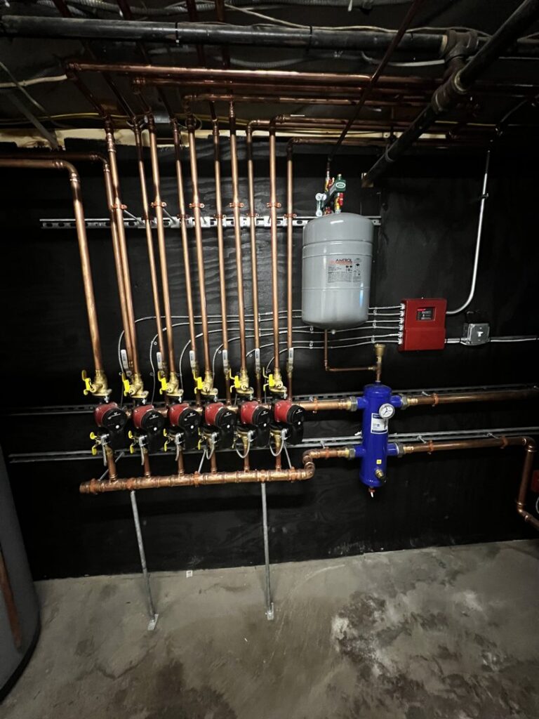 A detailed view of a hydronic heating manifold with copper pipes and pumps installed by All Points HVAC in Worcester, MA.