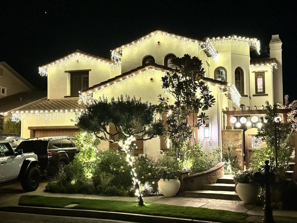 A house adorned with beautiful icicle Christmas lights and festive landscape lighting, installed by GL3 Luxury Lighting in Anaheim, CA.