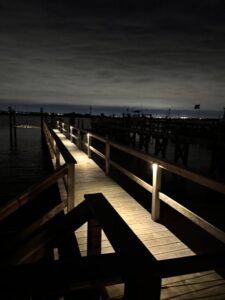 A long wooden dock beautifully illuminated by pathway lights at night, installed by New York Electrical Design in Freeport, NY
