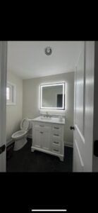 A modern bathroom featuring an illuminated mirror and recessed ceiling light installed by Mark Anthony Electric LLC in Wilmington, DE