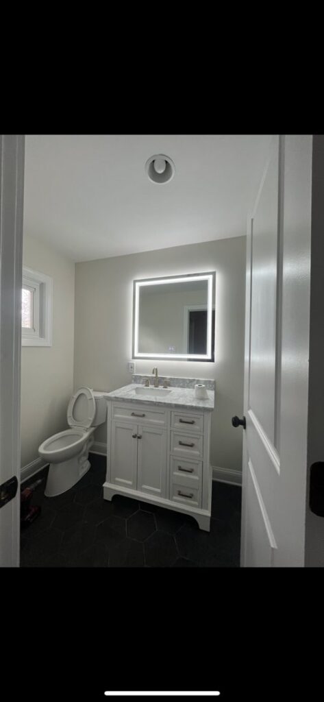 A modern bathroom featuring an illuminated mirror and recessed ceiling light installed by Mark Anthony Electric LLC in Wilmington, DE