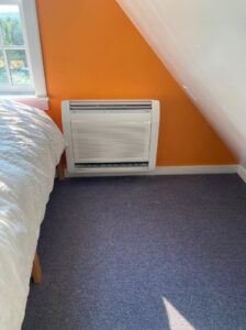 An indoor floor-mounted heat pump unit installed in a bedroom by Champlain Valley Heat Pump, LLC in Colchester, VT.