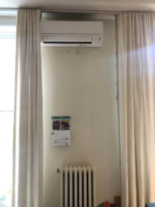 An indoor mini-split air conditioning unit installed above a window and radiator by ProMasters HVAC Mechanical in New York, NY