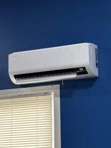 An indoor mini-split HVAC unit installed on a blue wall above a window by Bama Air Systems in Cullman, AL.