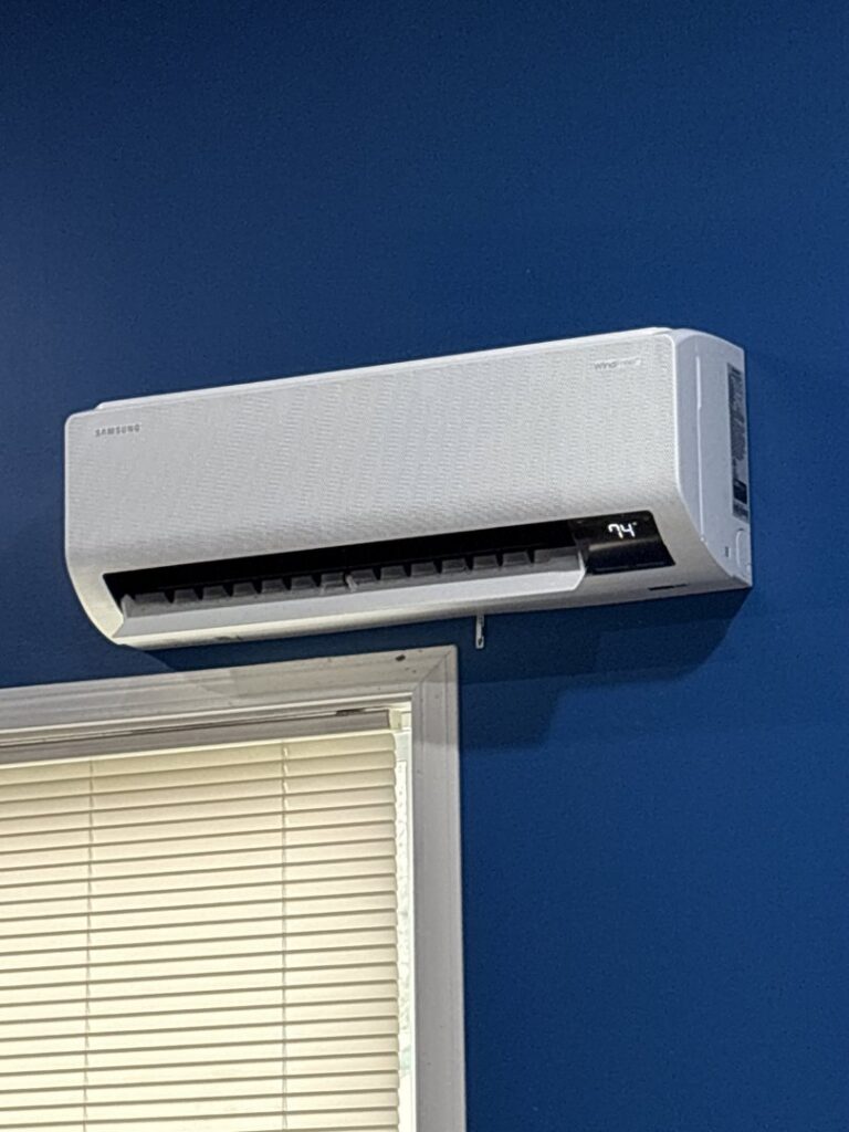 An indoor mini-split HVAC unit installed on a blue wall above a window by Bama Air Systems in Cullman, AL.