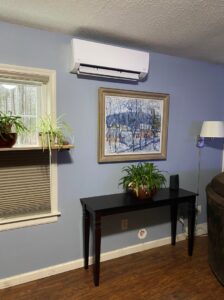 An indoor mini-split heat pump unit installed on a blue wall in a living room by Champlain Valley Heat Pump, LLC in Colchester, VT.