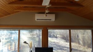 An indoor mini-split head unit installed high on a wall in a room with large windows by Custom Climates in Iowa City, IA.