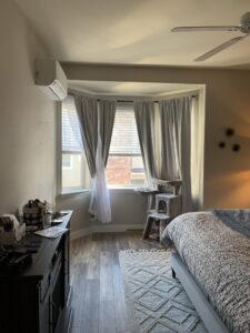 An indoor mini-split heat pump unit installed above a bay window in a bedroom by The Heat Pump Store in Portland, OR.