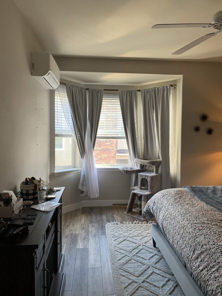 An indoor mini-split heat pump unit installed above a bay window in a bedroom by The Heat Pump Store in Portland, OR.