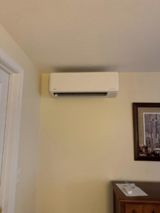 An indoor mini-split air conditioning unit installed on a yellow wall by Precision Heating and Gas Service in Derry, NH