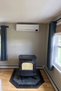 An indoor mini-split unit installed on a living room wall above a wood stove by Laird's HVAC in Auburn, ME.