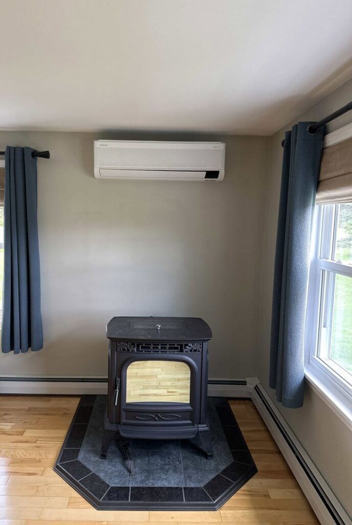 An indoor mini-split unit installed on a living room wall above a wood stove by Laird's HVAC in Auburn, ME.