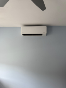 An indoor mini-split air conditioning unit installed on a light blue wall by Precision Heating and Gas Service in Derry, NH
