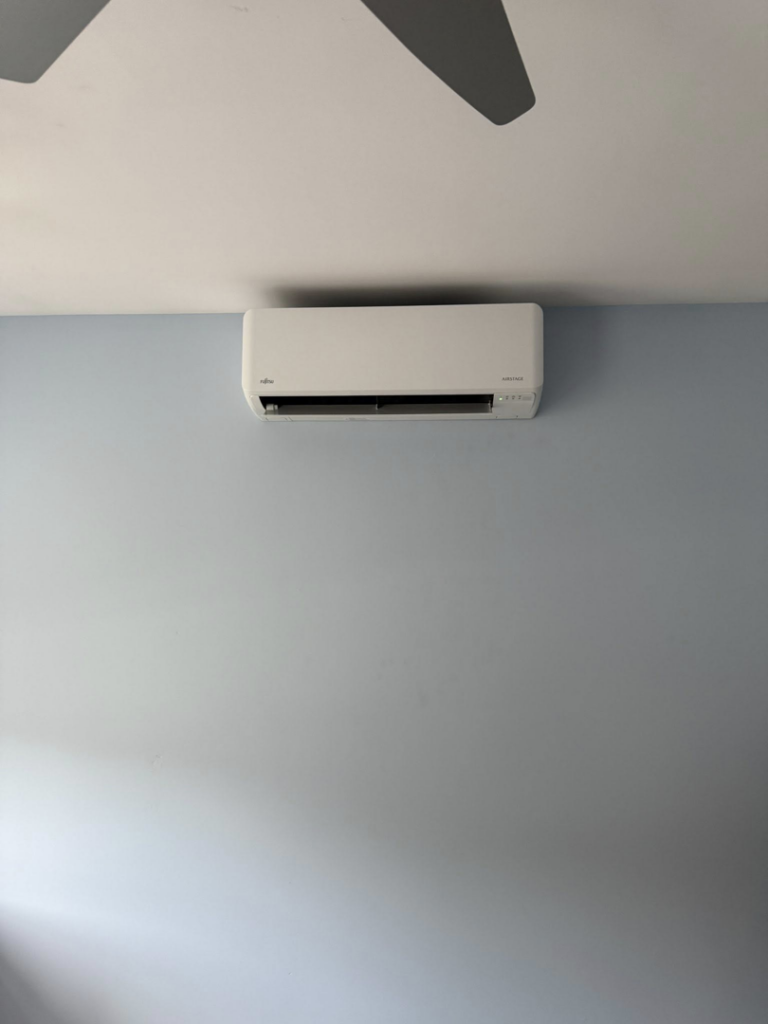 An indoor mini-split air conditioning unit installed on a light blue wall by Precision Heating and Gas Service in Derry, NH