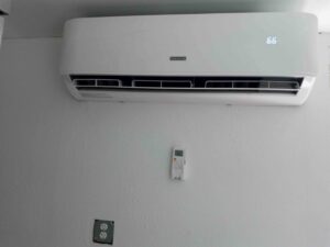 An indoor mini-split air conditioning unit mounted on a white wall with its remote control, installed by Jones Heating and Refrigeration in Dickinson, ND.