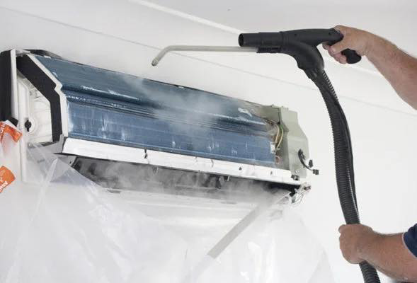 A technician cleaning an indoor split AC unit with a sprayer, providing maintenance from Noble Heating And Cooling in Wichita, KS.
