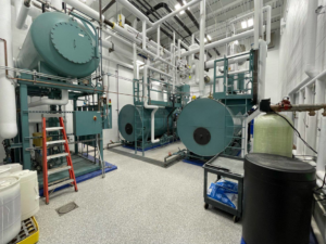 An industrial boiler room installation with multiple large HVAC units and extensive piping by Dean Boiler, Inc in Grand Rapids, MI.