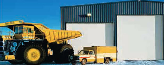 An industrial building with a large white garage door next to a yellow dump truck by Overhead Door Company of Knoxville in Knoxville, TN