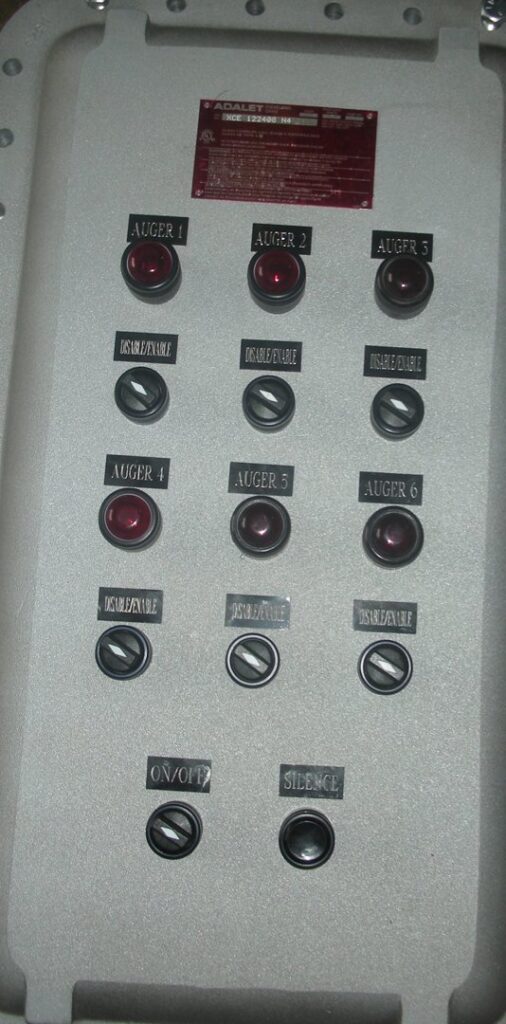 An industrial control panel with multiple "Auger" and "Disable/Enable" buttons, representing electrical control work by Basic Supply in Lafayette, LA.